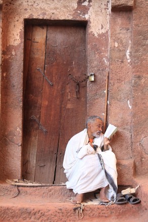 Hermit reads from his bible on the steps of a Lalibela church
